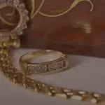 Goldener Diamantring und edle Goldkette vor einer verzierten Holzschatulle.