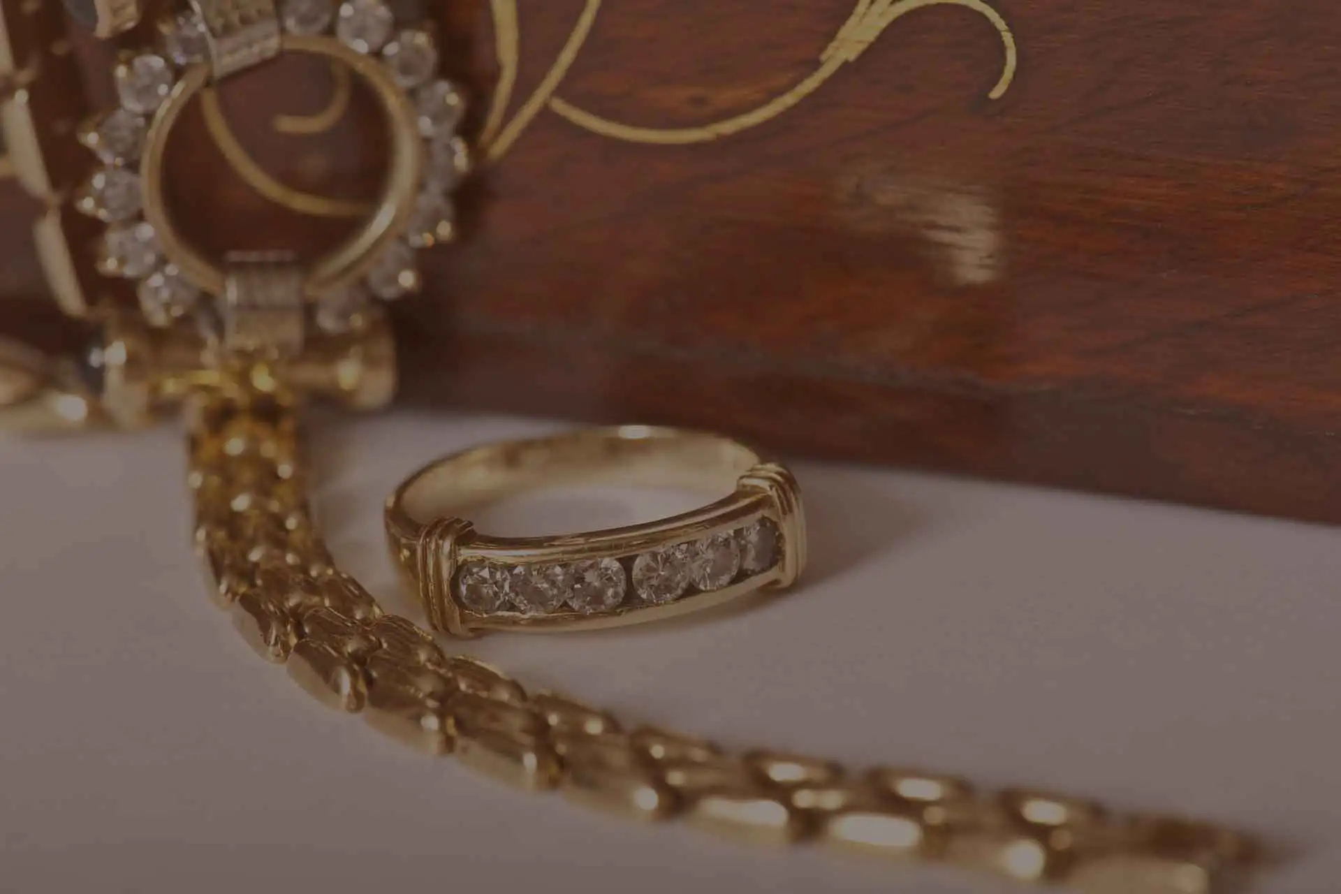 Goldener Diamantring und edle Goldkette vor einer verzierten Holzschatulle.