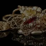 Angesammelter Goldschmuck, Ketten und Anhänger mit Edelsteinen auf einer spiegelnden, schwarzen Oberfläche.