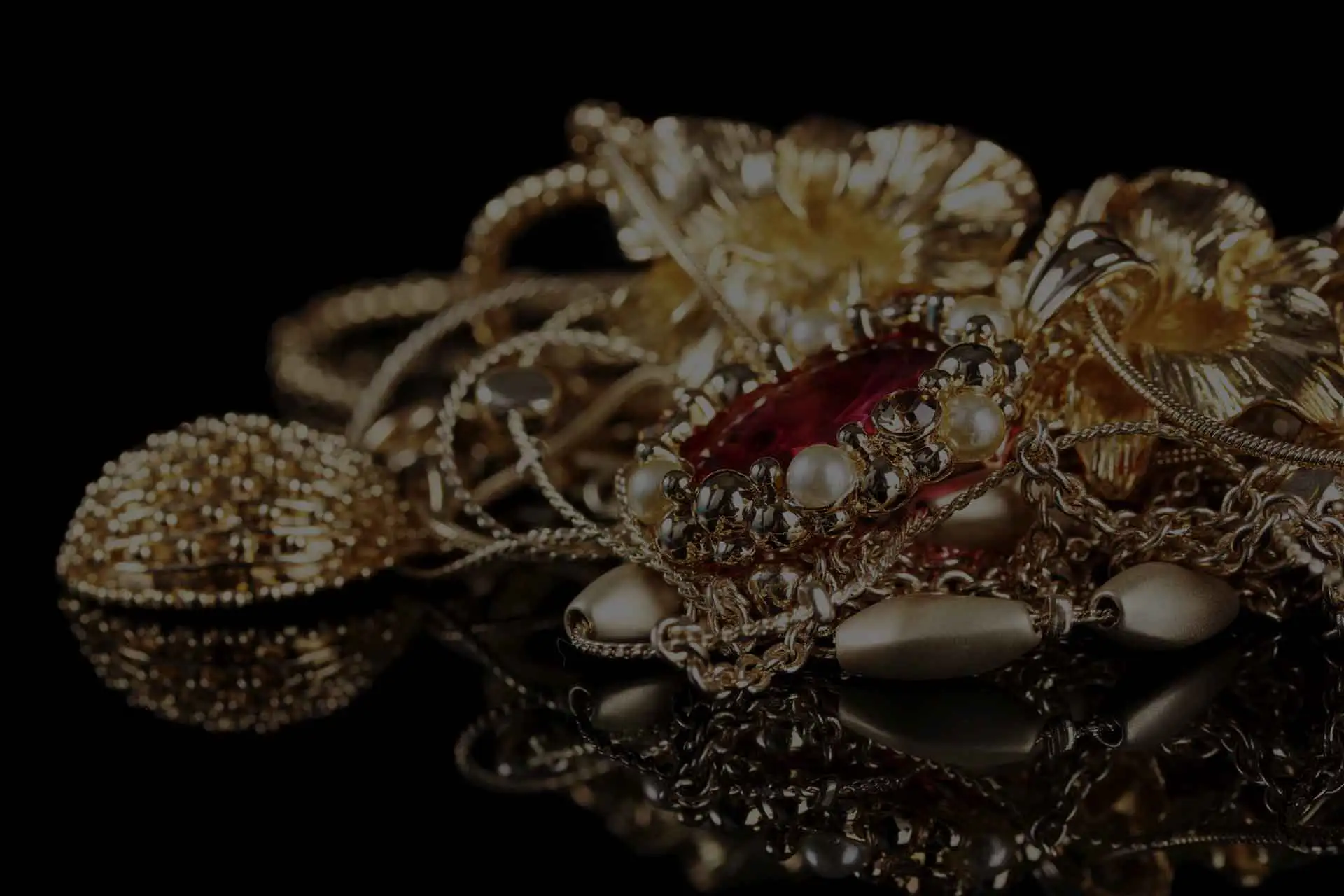 Angesammelter Goldschmuck, Ketten und Anhänger mit Edelsteinen auf einer spiegelnden, schwarzen Oberfläche.