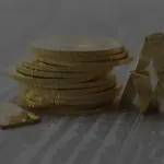 Stapel aus Goldmünzen und kleine Goldbarren von Umicore und Heraeus als Kartenhaus auf Kursnotierungen einer Zeitung.