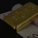 Ein 250g Feingoldbarren liegt auf gerollten Euro-Geldscheinen auf dunklem Grund.